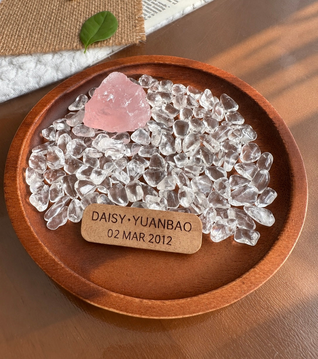 Raw rose quartz and clear quartz chips in a walnut wood dish with an engraved wooden tag.