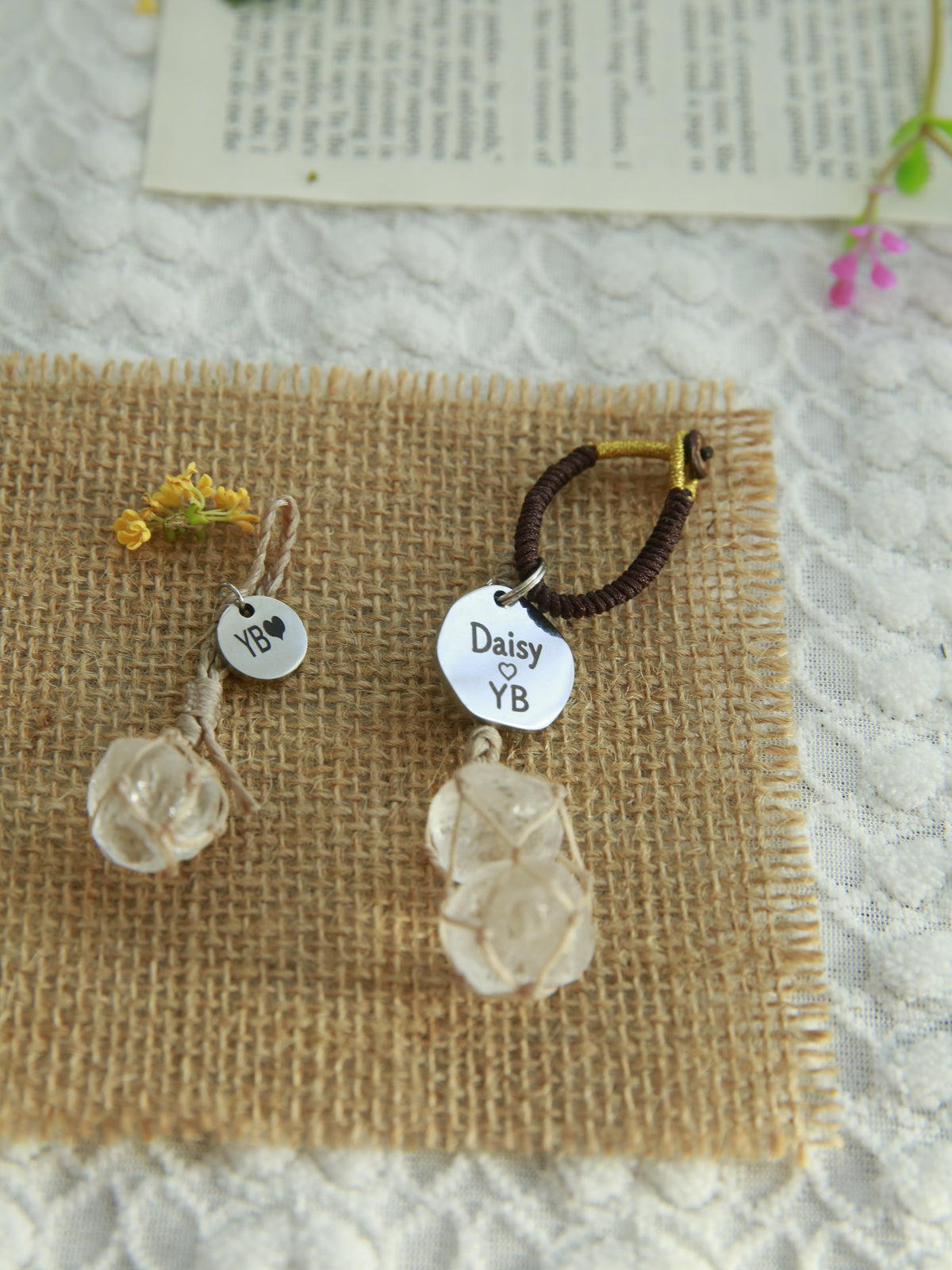 Beige Clear Quartz pet pendant beside a matching double Clear Quartz owner bag charm, showing both engraved name tags on burlap