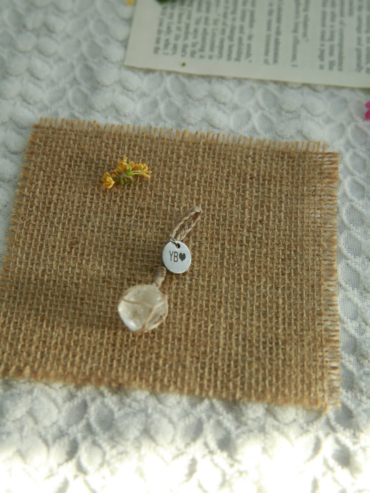 Single raw Clear Quartz pet pendant with beige waxed cord and a personalized 12mm round tag on woven burlap