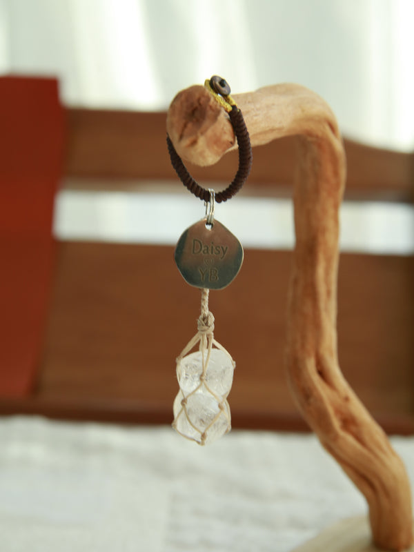 Two clear quartz stones held in a beige waxed cord net beneath an engraved owner tag