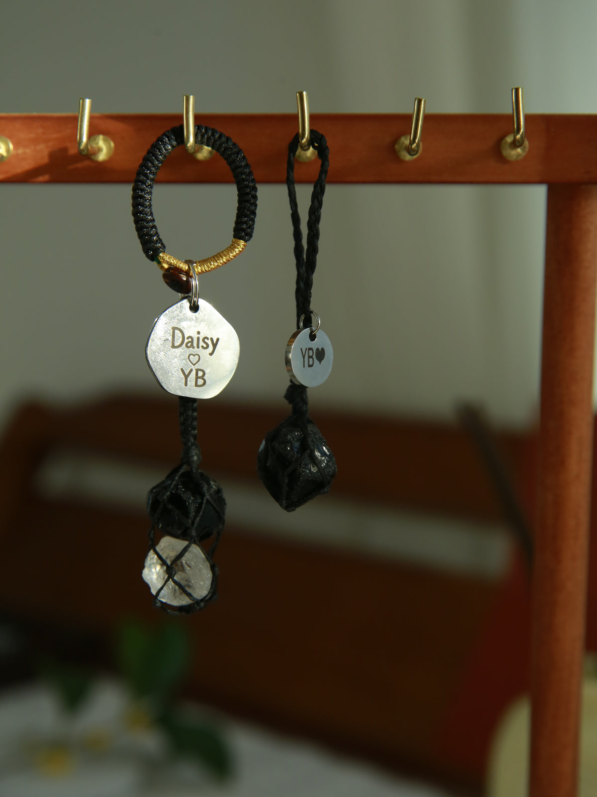Front view of the matching black obsidian pet pendant and obsidian and Clear Quartz owner charm hanging from a wooden rack, with engraved name tags