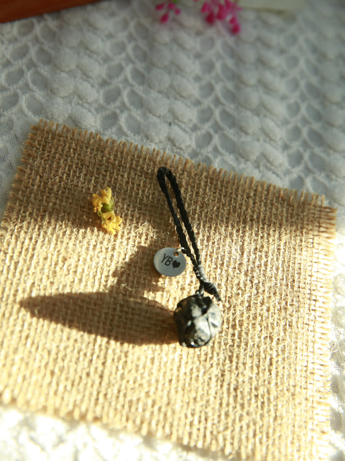 Handwoven Black Obsidian pet pendant with a personalized round tag and adjustable black waxed cord collar loop on burlap